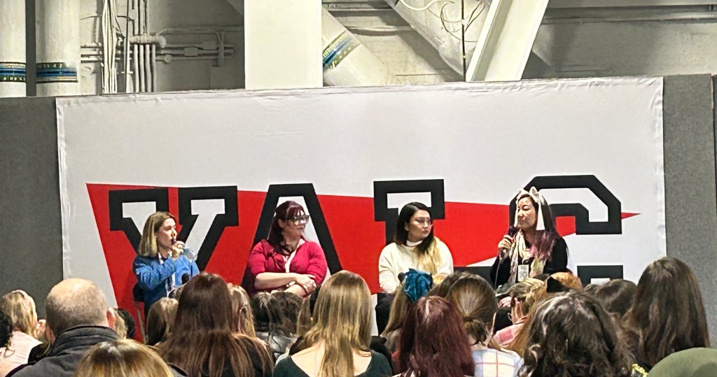 cropped image of a panel of 4 authors in front of an audience with the YALC sign behind them
